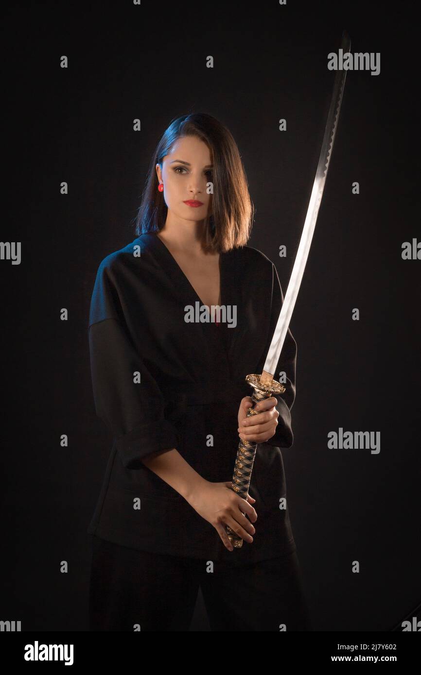 Portrait of a young brunette kung fu girl with a Japanese sword on a black background Stock Photo