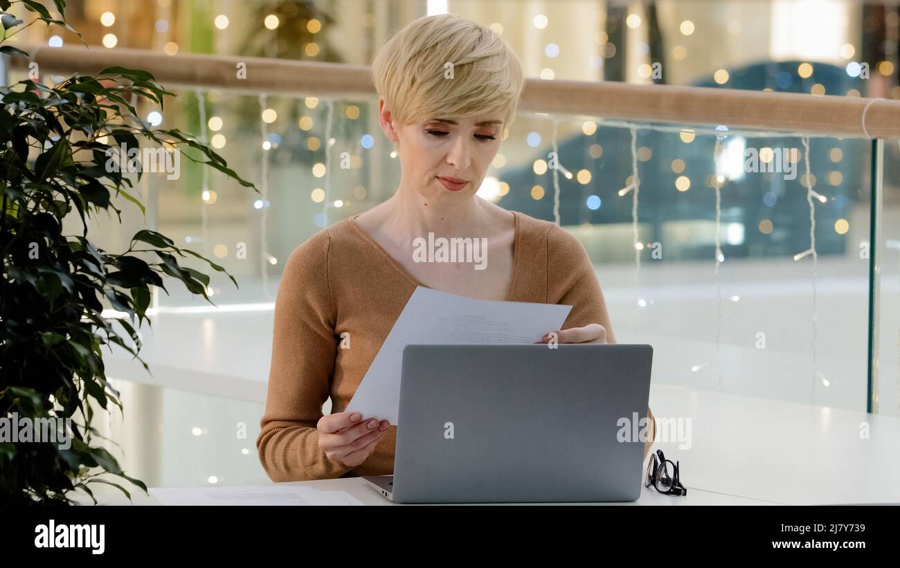 Caucasian middle aged business woman teacher freelancer paperwork sitting table with laptop paperwork feeling frustrated angry due to mistake in Stock Photo