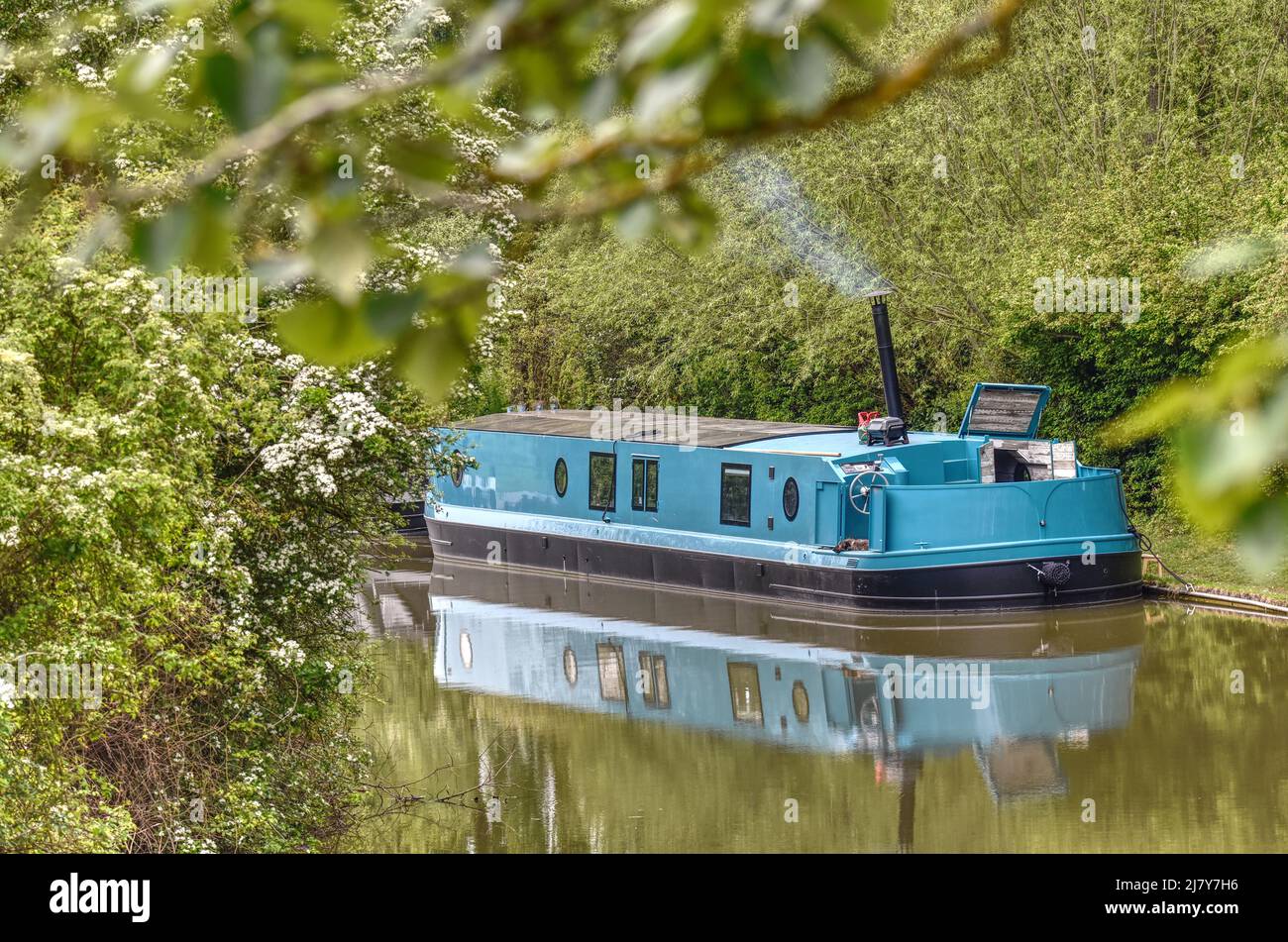 A wisp of smoke rises from a narrowboat moored along the beautiful Grand Union Canal in Milton Keynes Stock Photo