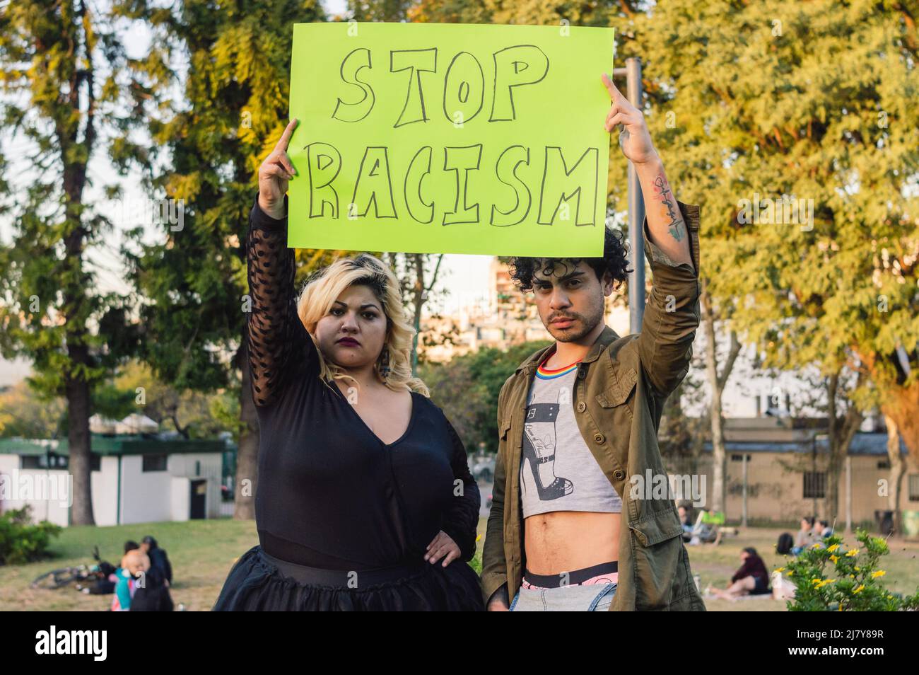 young plus size woman and homosexual man, outdoors in a public park, protesting holding a sign that says 'stop racism' Stock Photo