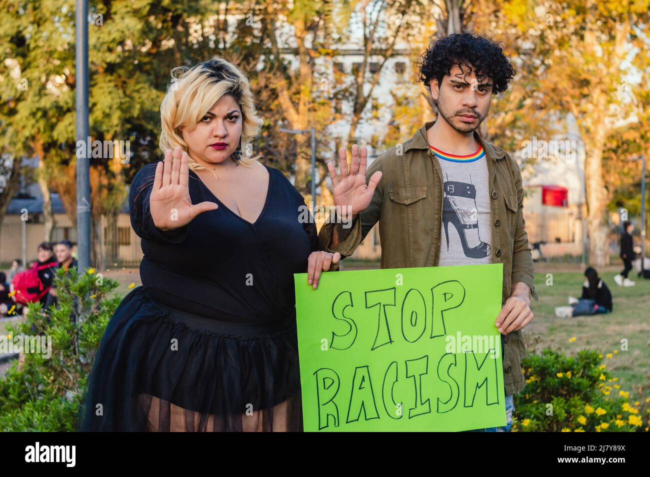 young, serious caucasian man and woman protesting in the park with hands on stop, holding sign that says 'stop racism', inclusive concept. Stock Photo