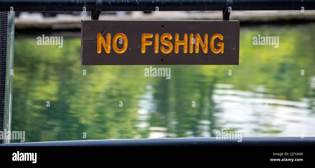 A rectangular wooden sign with orange lettering announces that fishing is not allowed here. Bokeh effect. Stock Photo