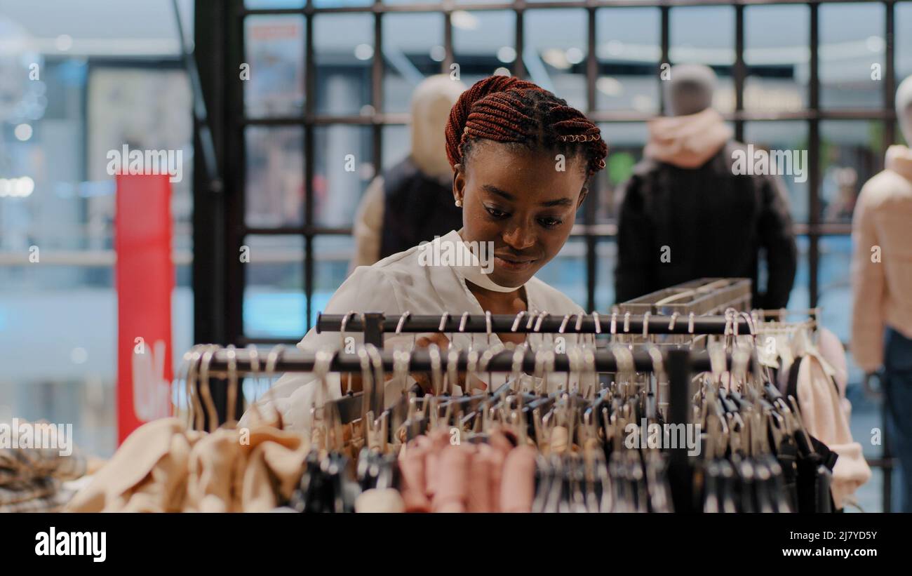 Young beautiful stylish shopper female consumer african american woman girl looking for perfect clothes in clothing store choosing luxury dress goods Stock Photo