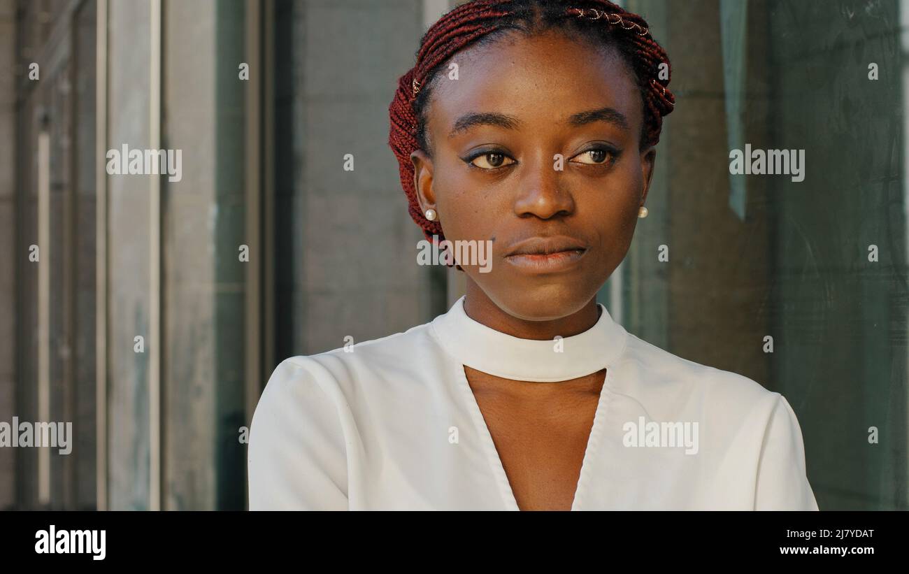 Close-up female portrait african american girl lady woman student businessperson face stylish model stands in city on building background looking into Stock Photo