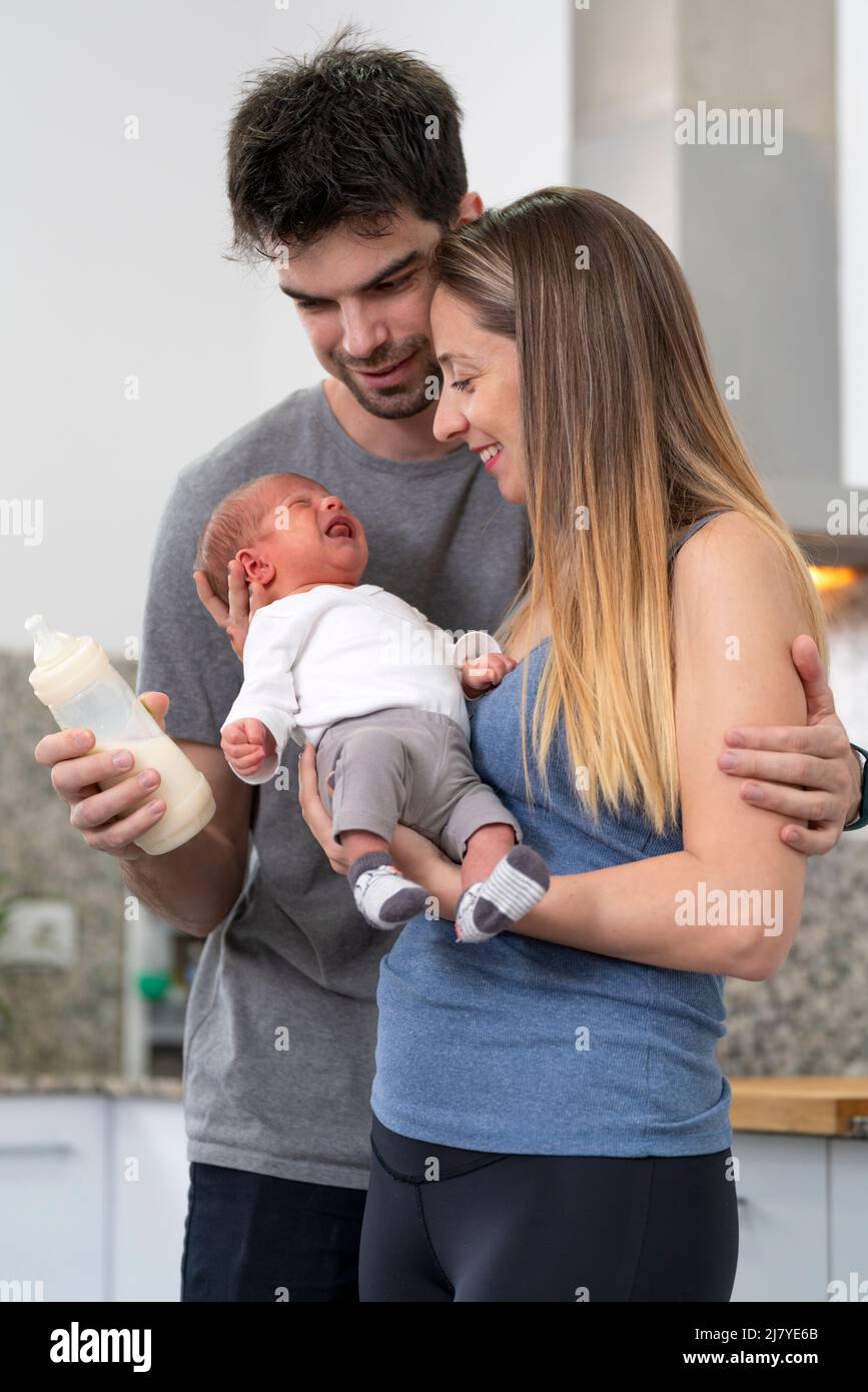 mother and father bottle feeding their newborn baby in the kitchen Stock Photo