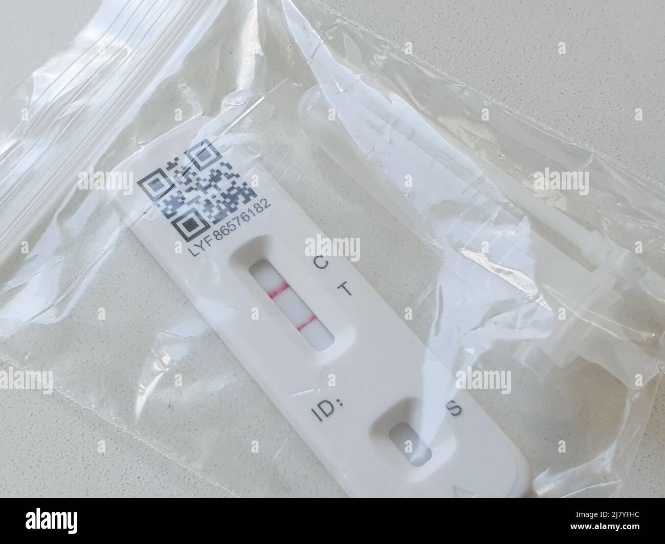 A lateral flow test positive for covid. The rapid antigen test is in a plastic bag with the swab and extraction buffer tube, ready for disposal. Stock Photo