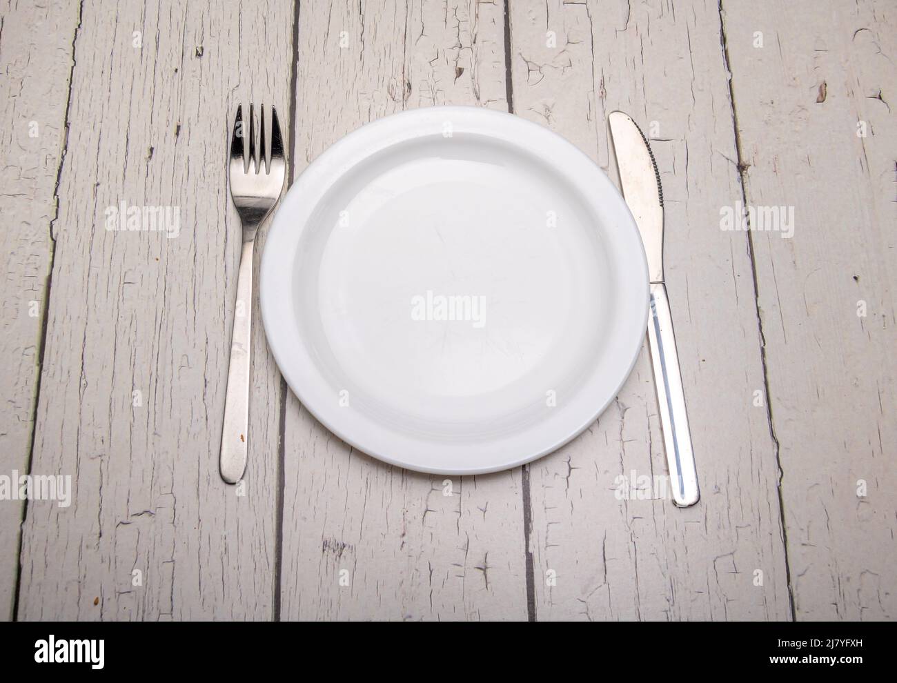 A empty plain white plate and cutlery with signs of use on a rustic