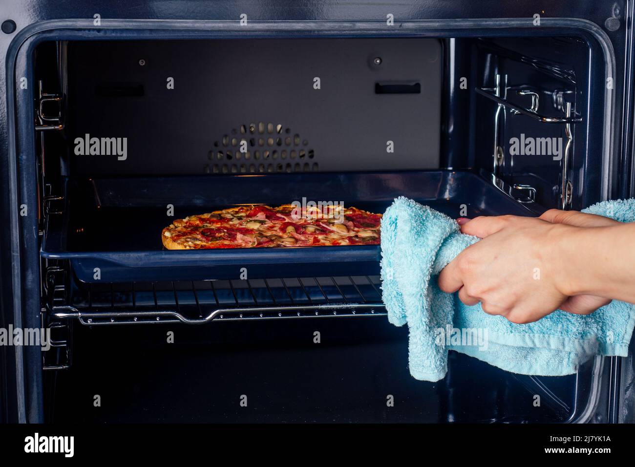 woman openung ovens and take pizza with tomatoes, olives, mushrooms and cheese sausage Stock Photo