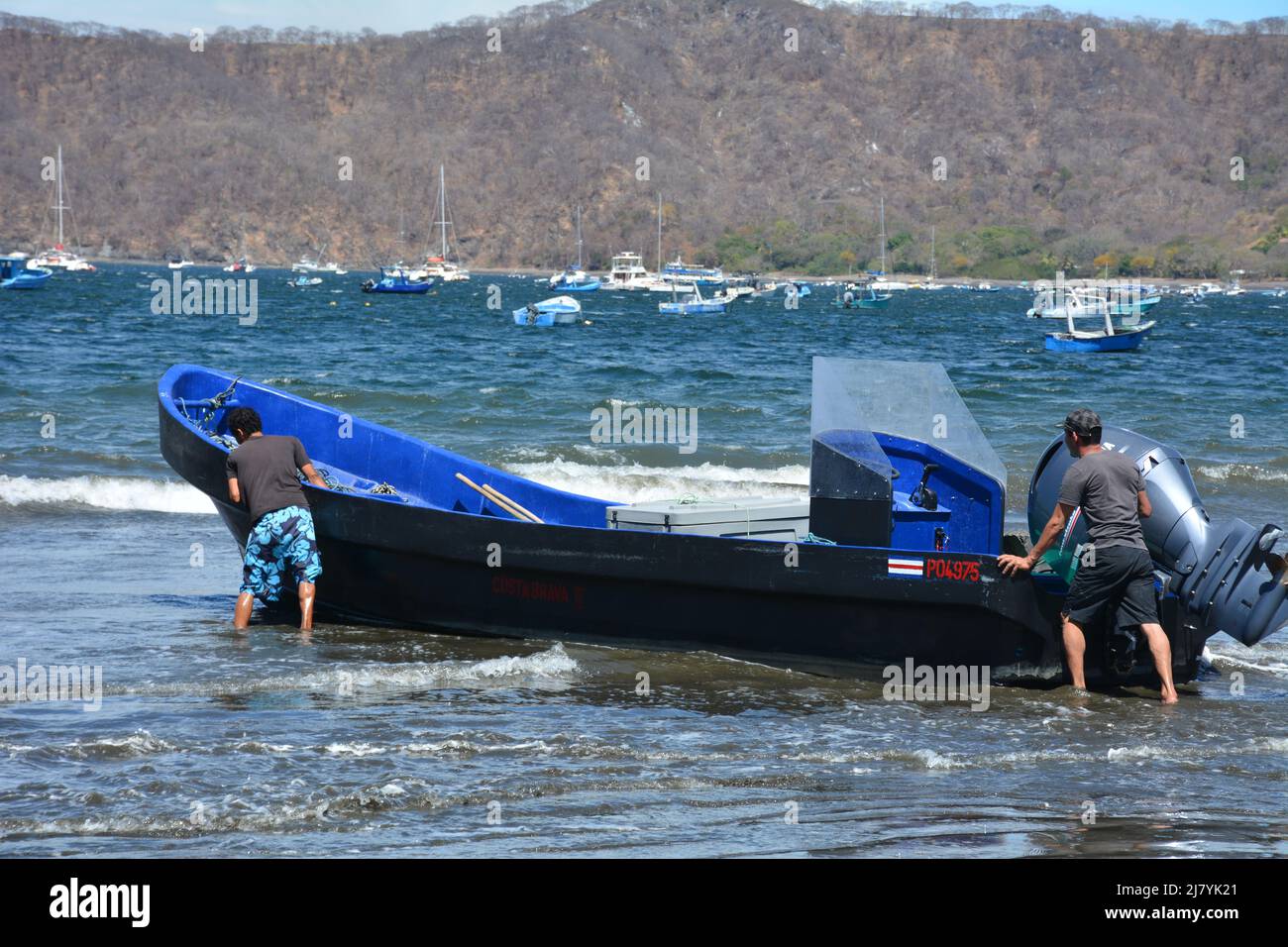 Men pushing  boat into surf on Costa Rican beach Stock Photo