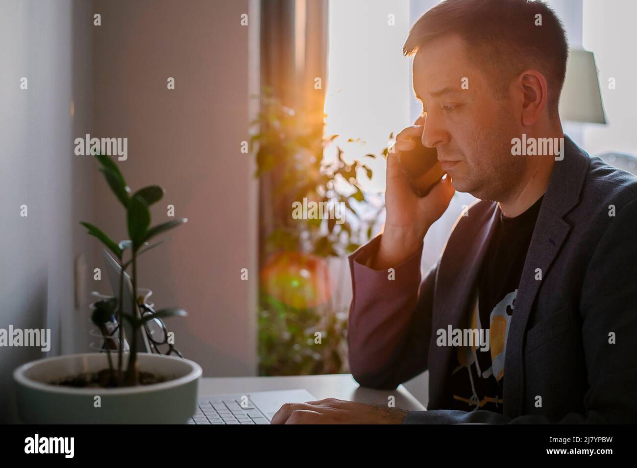 Man working remote job from home office. Cheerful freelancer working on laptop and talking on the phone Stock Photo