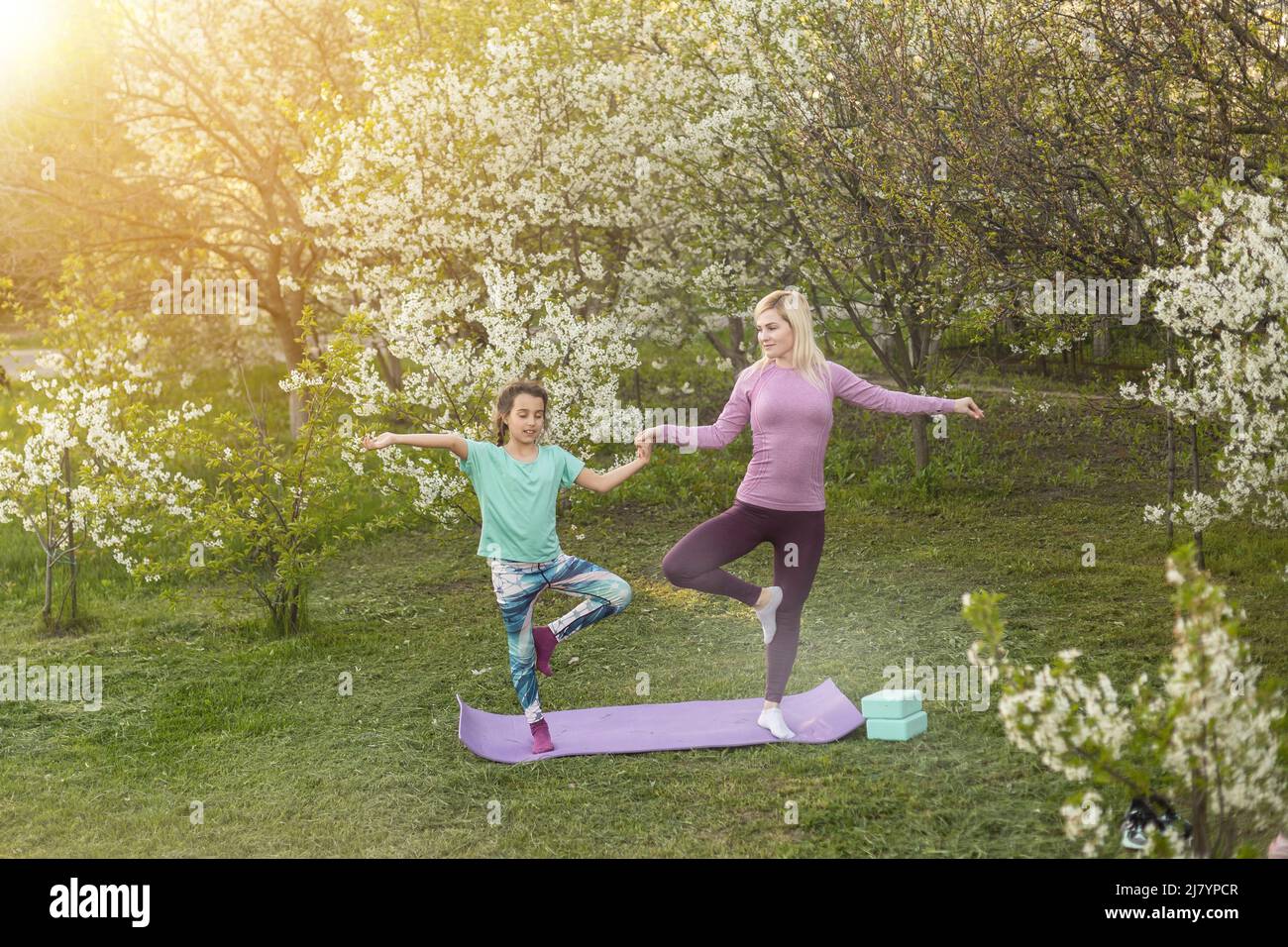 a young mother and daughter perform yoga exercises in the park on a gym mat. healthy lifestyle. Stock Photo