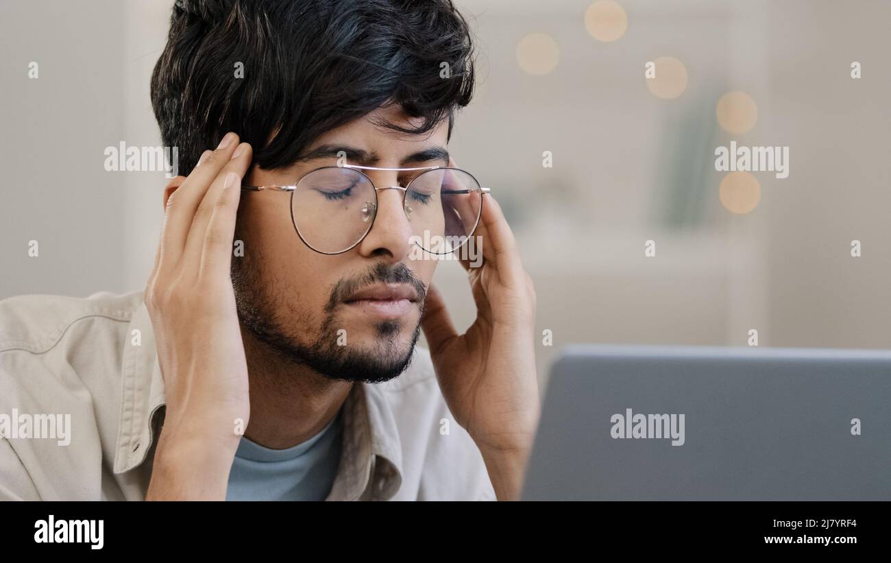 Close-up arab business man student male bearded boss leader with glasses guy works with laptop problems suffers from headache massages head feeling Stock Photo