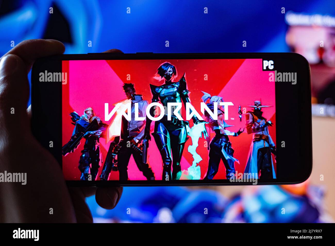 Valorant Game Title is shown on mobile phone Screen with twitch Streamer playing game in the background. A Game made by Riot Games in Los Angeles. Stock Photo