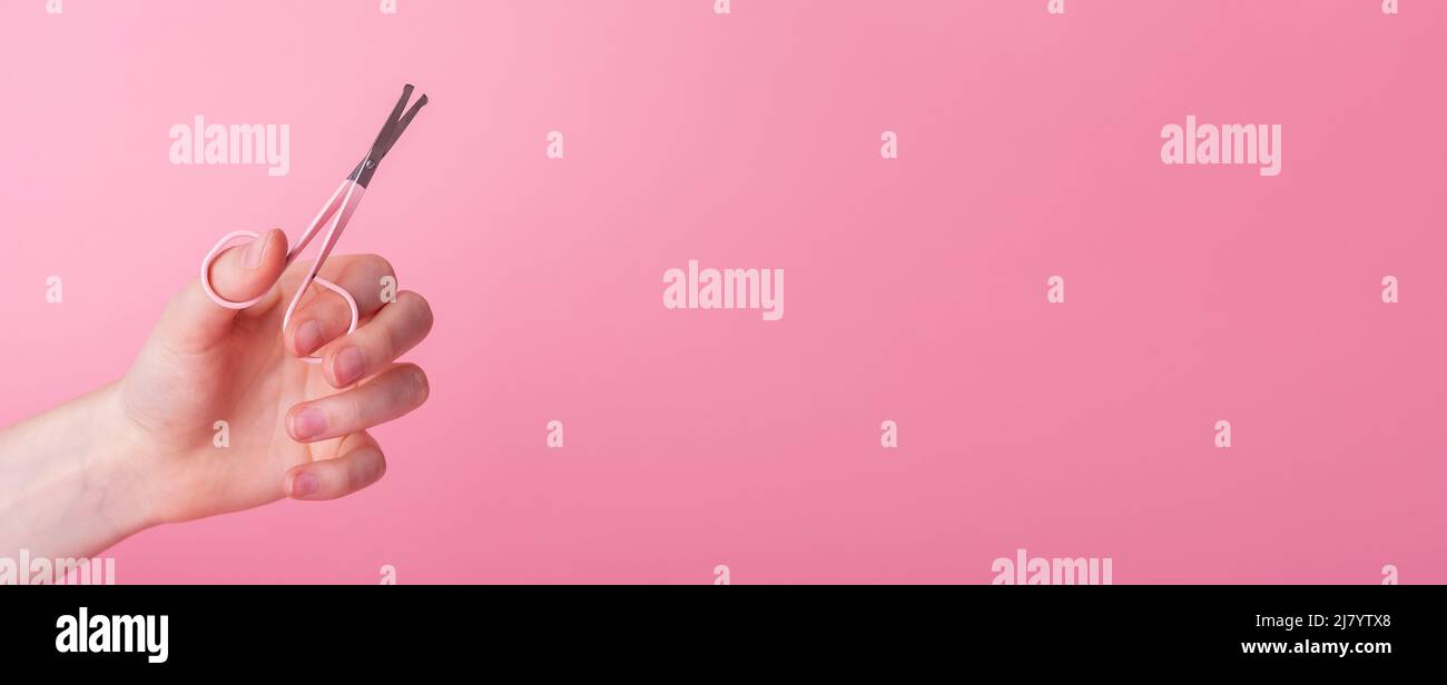 Nail manicure scissors in hands on pink background. Banner with copy space for text. High quality photo Stock Photo