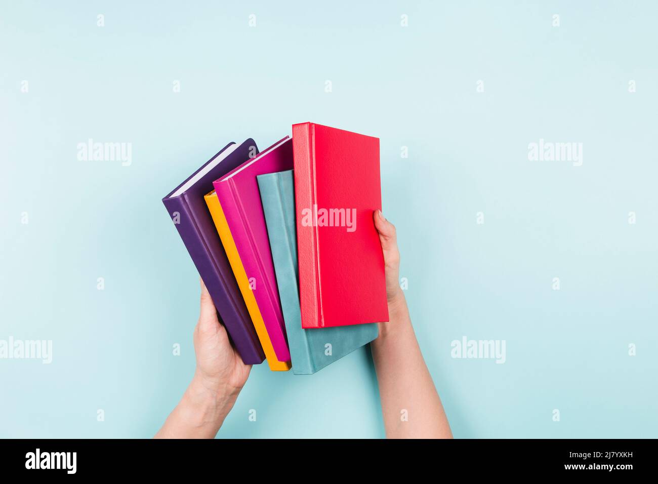 Female hands holding pile of books over light blue background. Education, self-learning, hobby, relax time at home Stock Photo