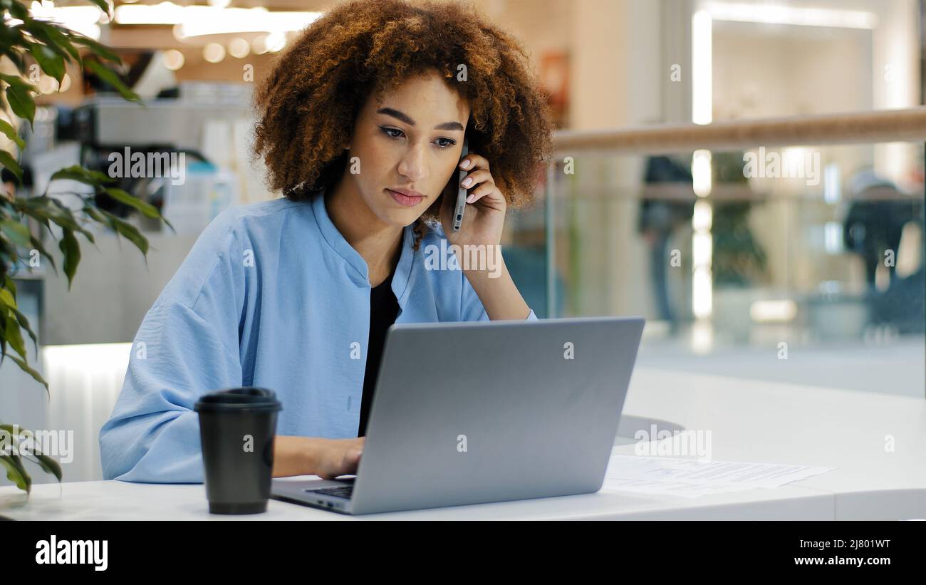 African american busy business woman freelancer girl manager boss female leader worker talking by mobile phone answering call writes notes working Stock Photo