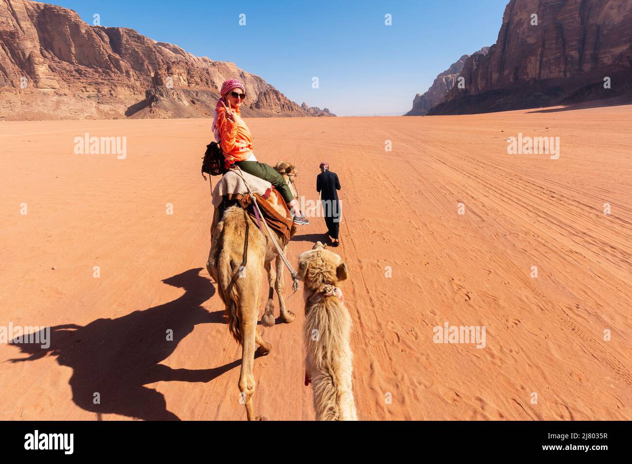 beautiful young woman tourist in white dress riding on camel in wadi rum desert, Jordan Stock Photo