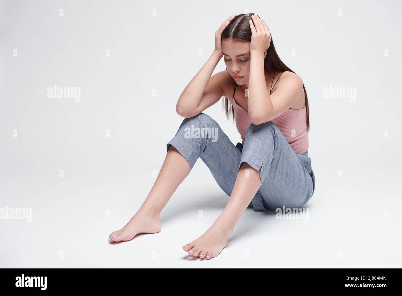 Emotionally exhausted girl having panic attack sitting on floor and holding head in