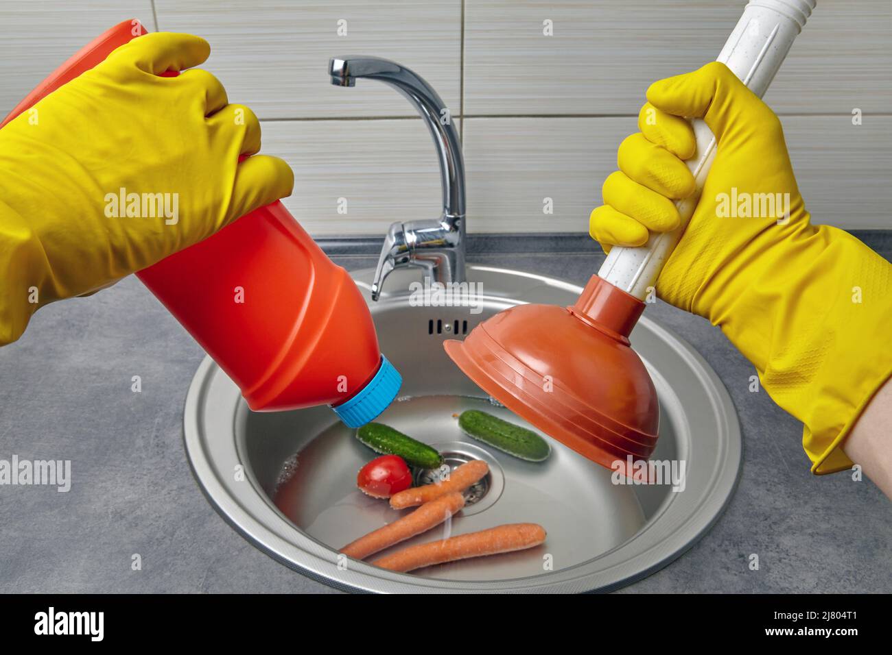 Hands in yellow rubber gloves hold a plunger and pipe cleaner against