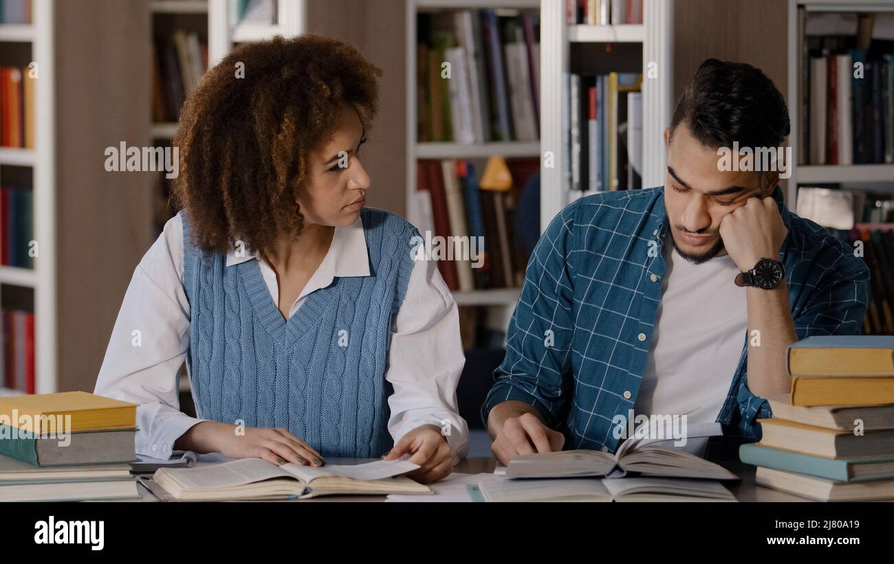 Two students guy and girl sitting at desk classroom writes notes in notebook writing information from textbook reading book young male student falls Stock Photo