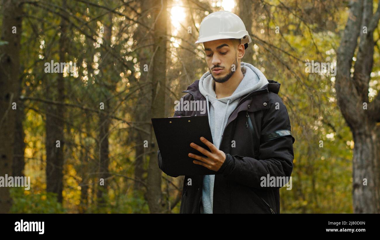 Young experienced Indian man forestry engineer in hardhat with tablet taking measures for reforestation of woodlands. Working and Supervising in park Stock Photo