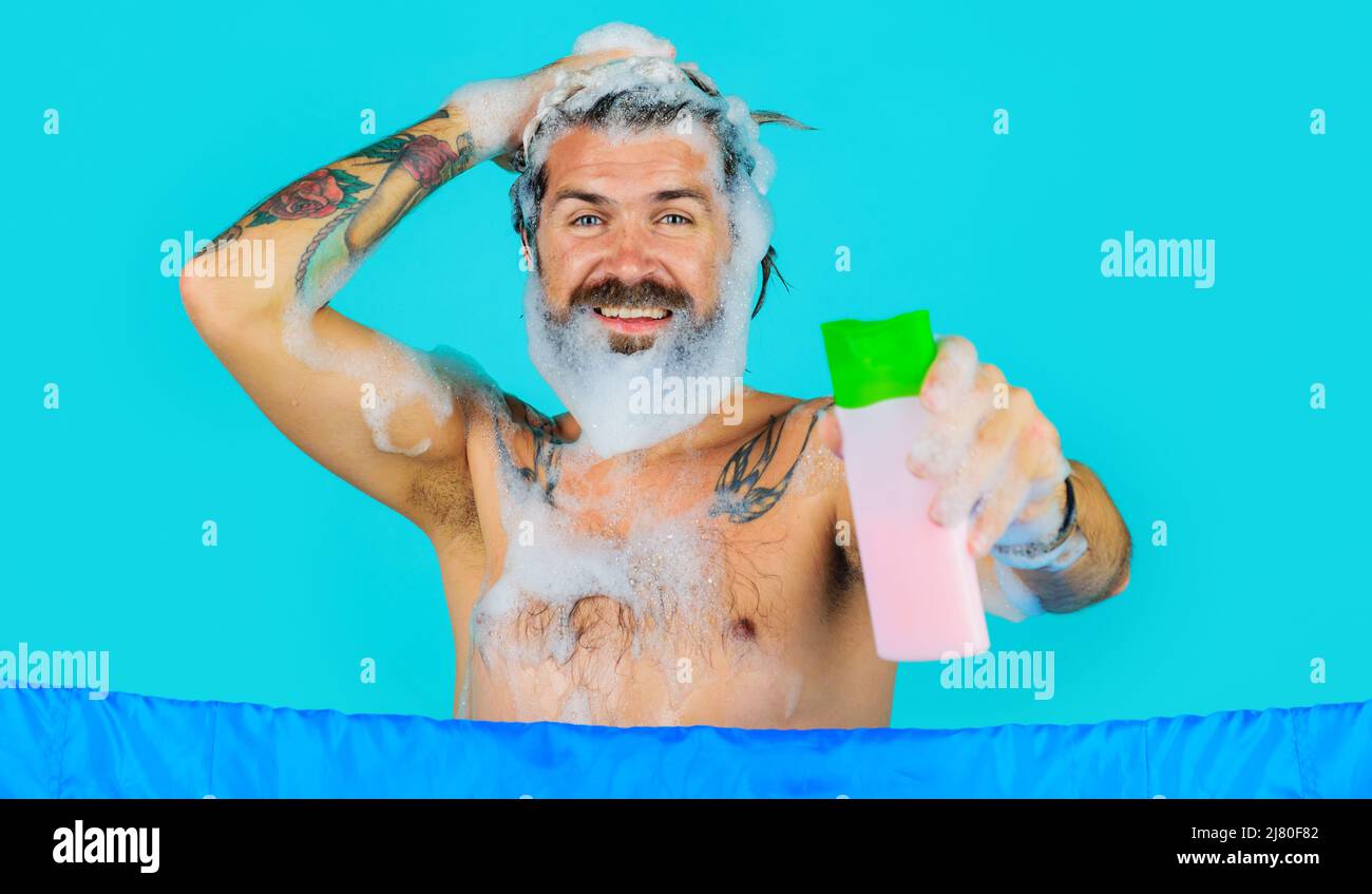 Bearded man in shower with shampoo bottle. Happy guy with foam on head