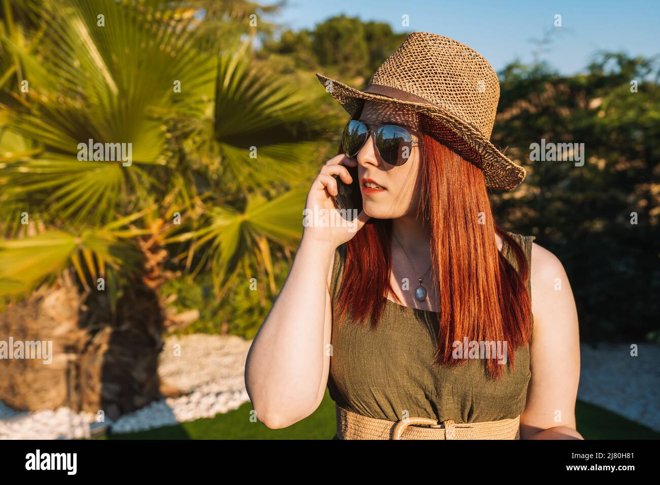 young red-haired woman travelling, calls her family on her mobile phone when she arrives at her holiday destination. Stock Photo
