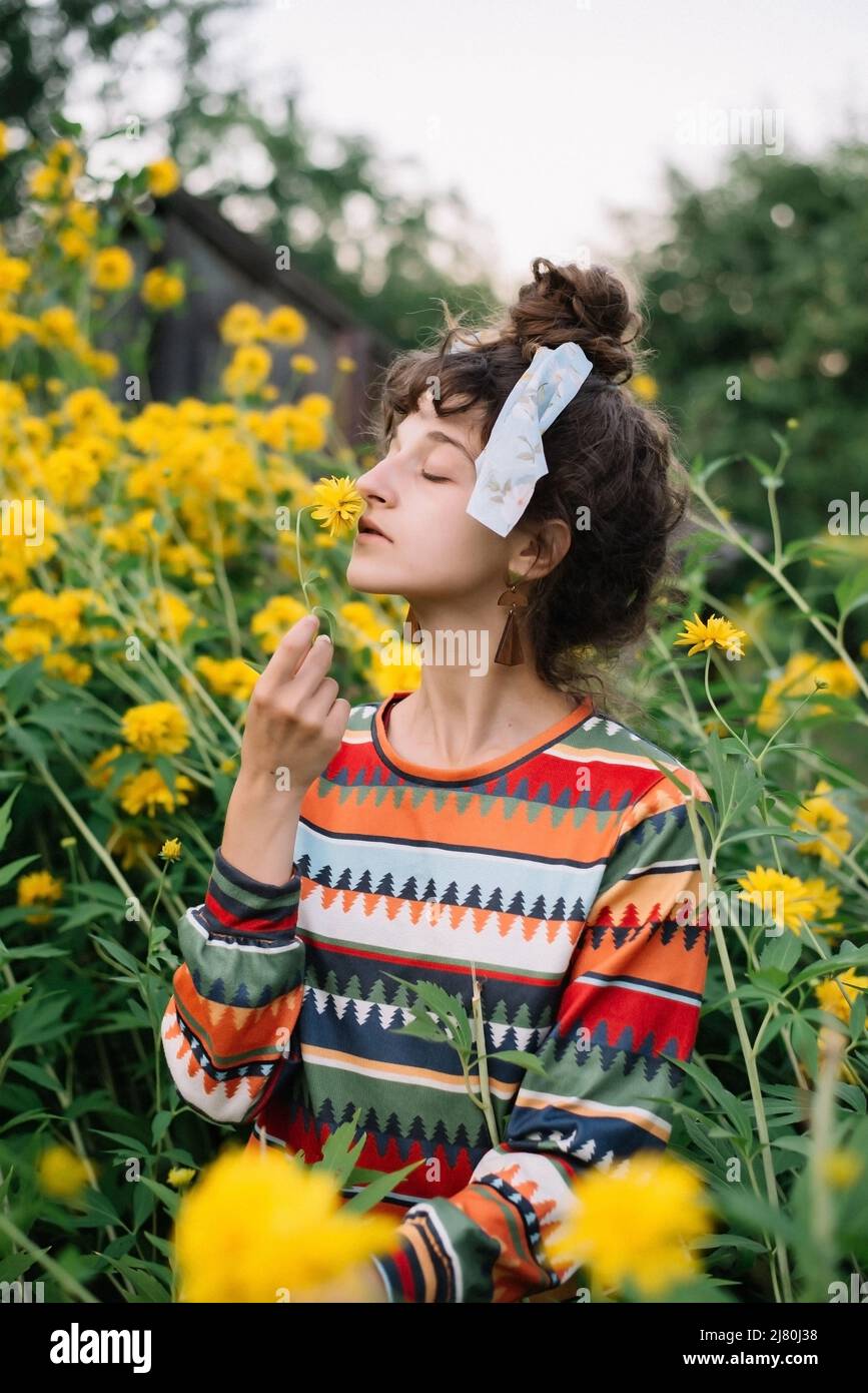 Pensive hippie woman wearing colorful clothes sniffs a yellow fl Stock Photo