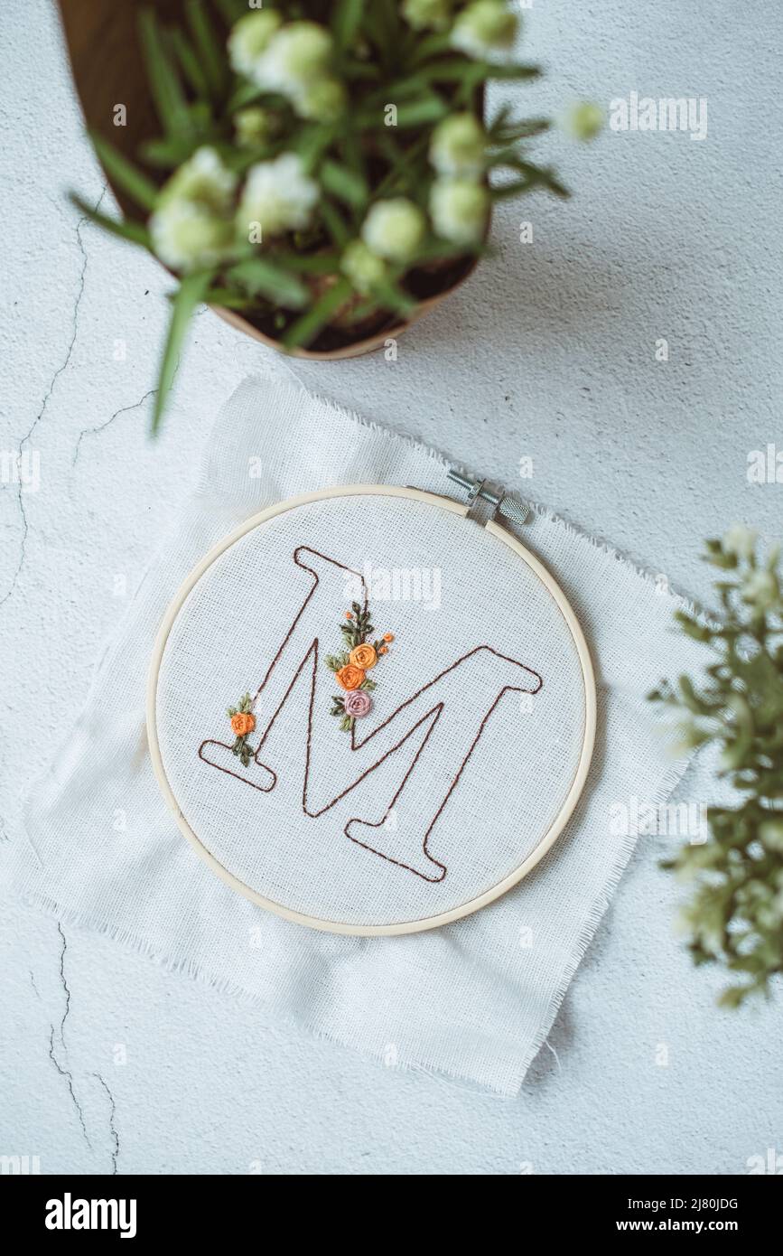 Overhead view of an embroidery hoop with the letter M on a table next to a  bunch of flowers Stock Photo - Alamy