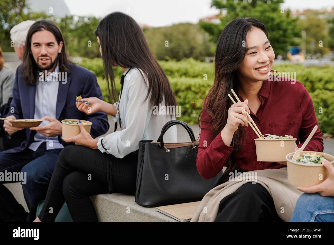 Multiethnic business people eating takeaway food during lunch break outdoor outside the office - Focus on Asian woman face Stock Photo