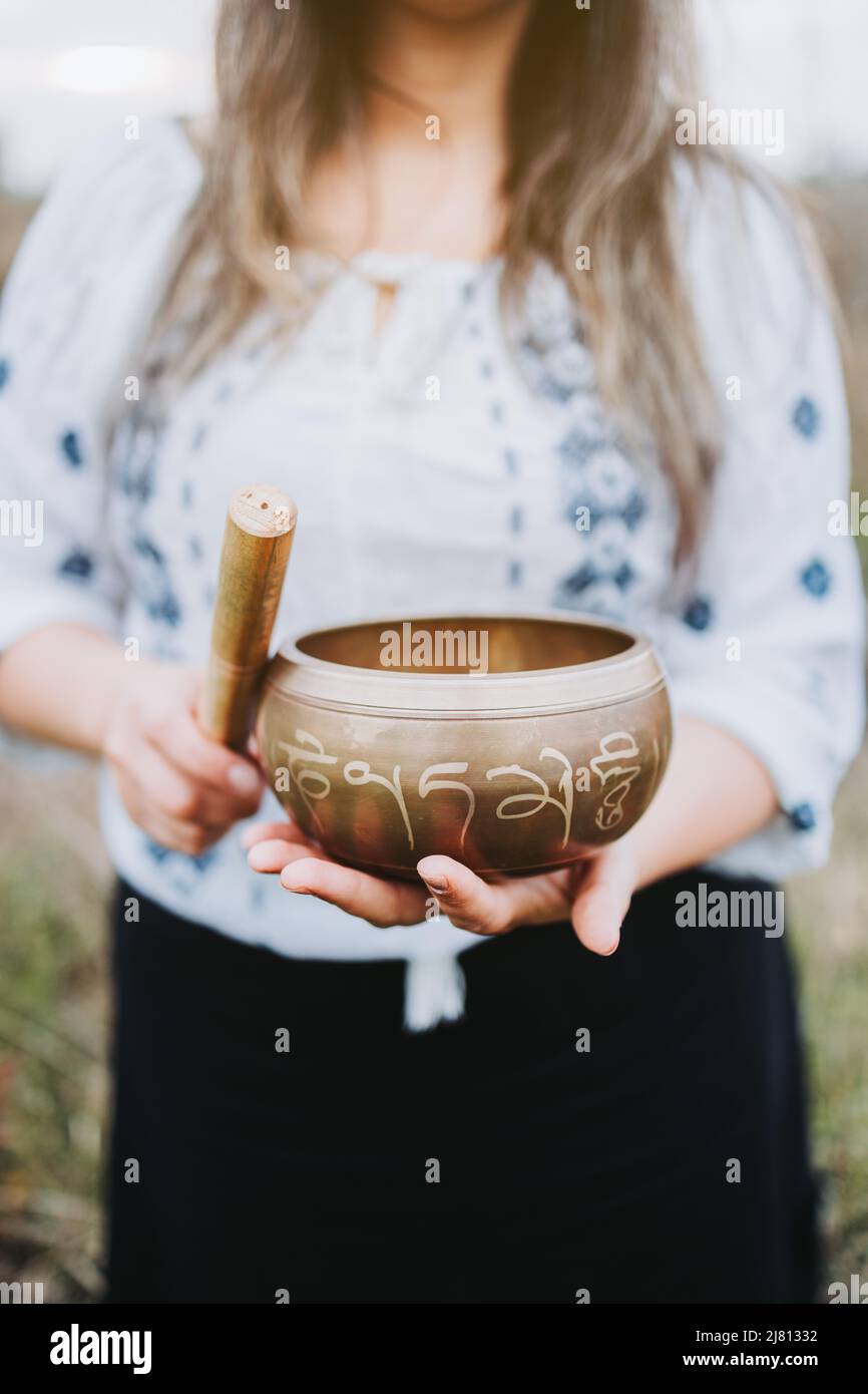 Blonde woman holding a tibetan singing bowl with a wooden stock. Selective focus Stock Photo