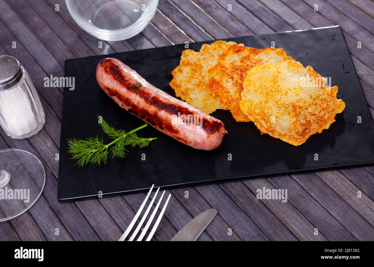 Fried potato pancakes on black slate board with grilled sausage Stock