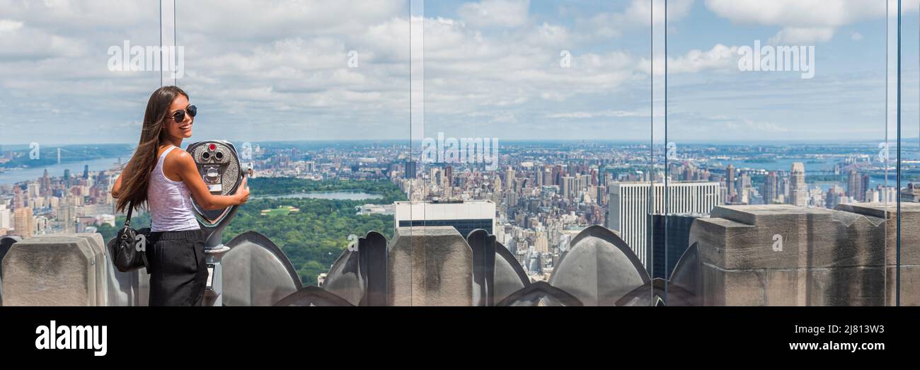 USA travel tourist in New York City vacation- woman looking at view of skyline with binoculars from skyscraper. Girl traveling summer holidays United Stock Photo