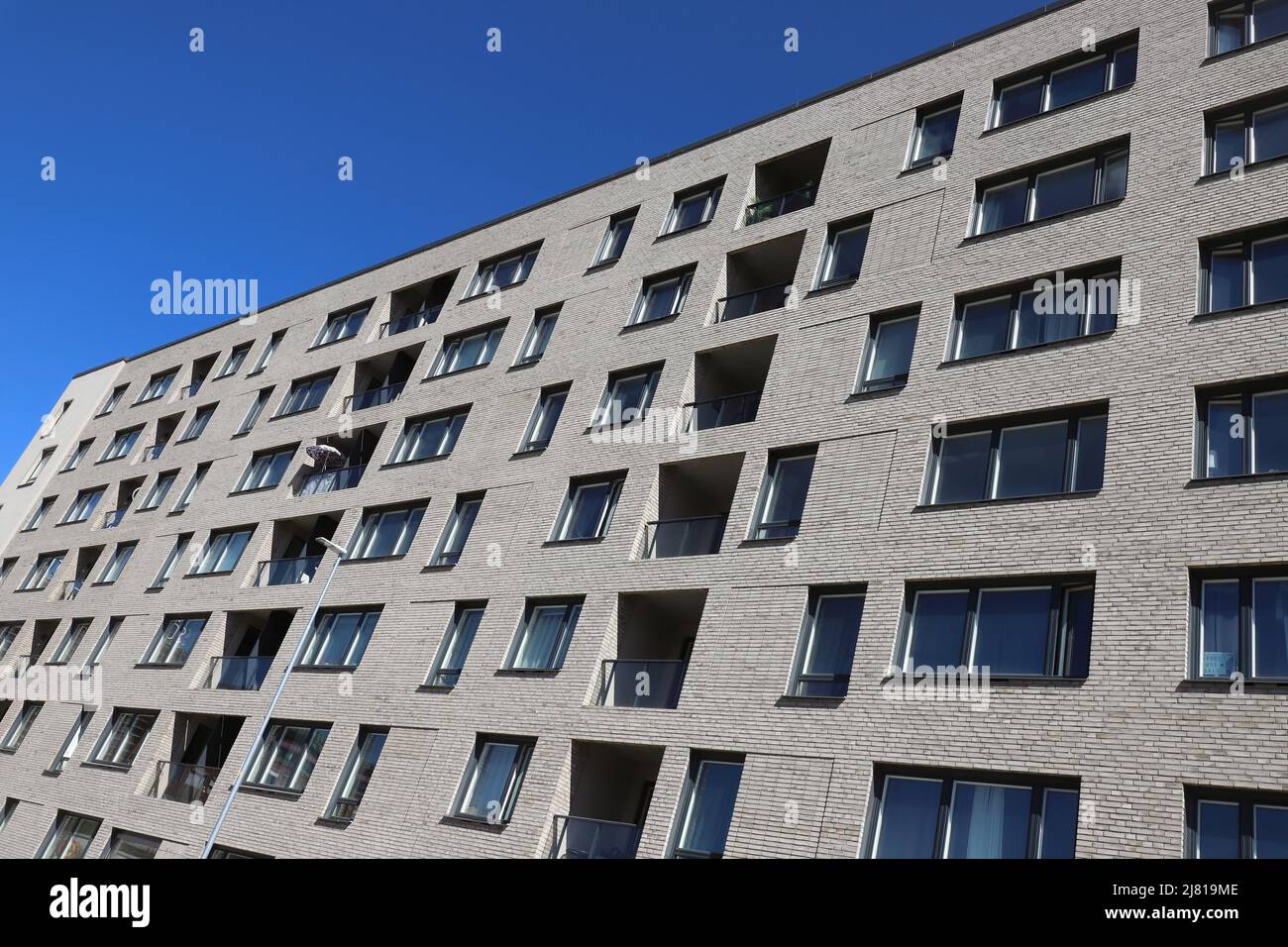 Low angle view of a modern multi-story residential apartment buildning against a clear blue sky. Stock Photo