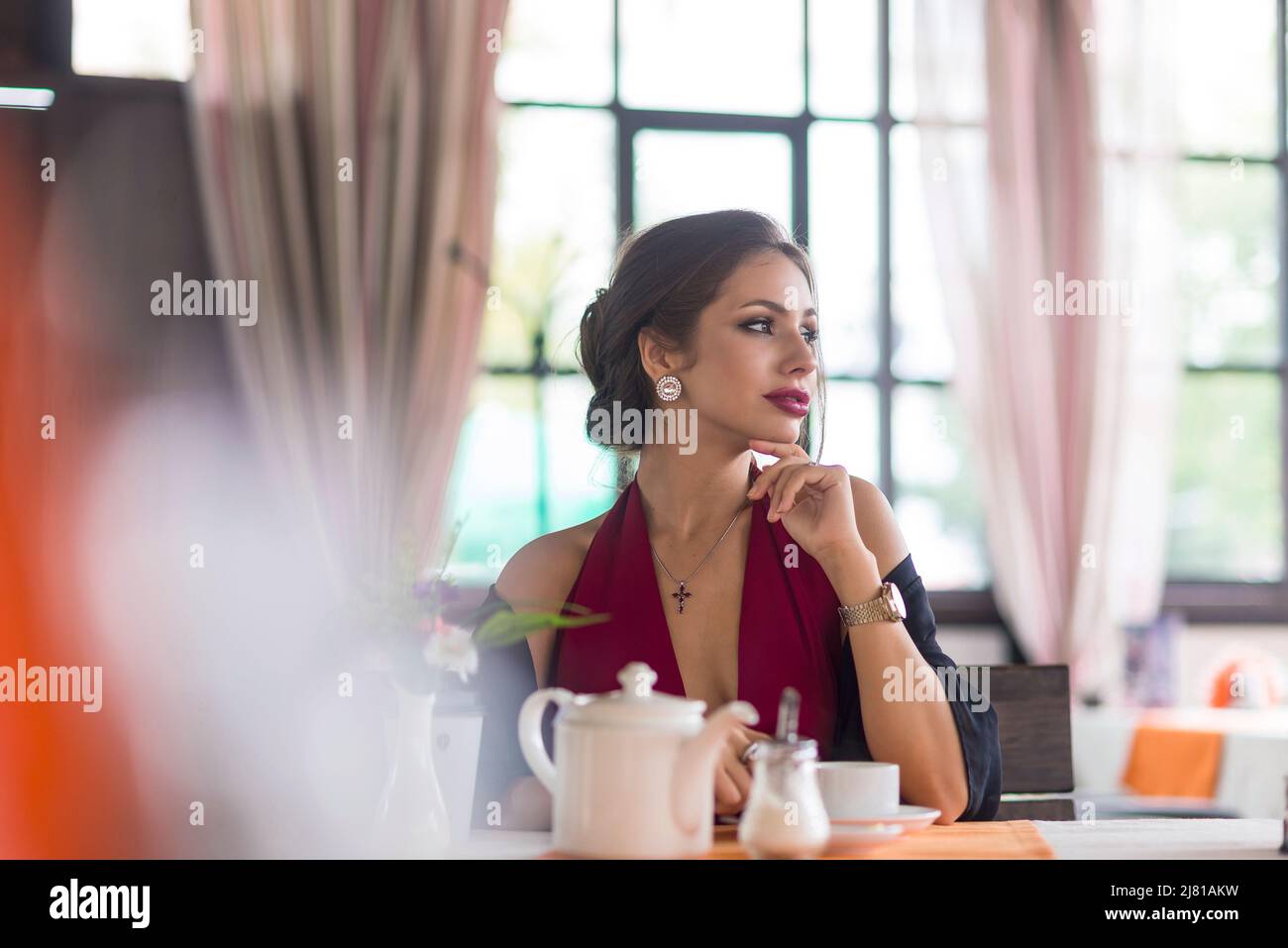 Stylish young woman drinking tea or coffee at a cafe. She enjoys the taste and looking by side. Stock Photo