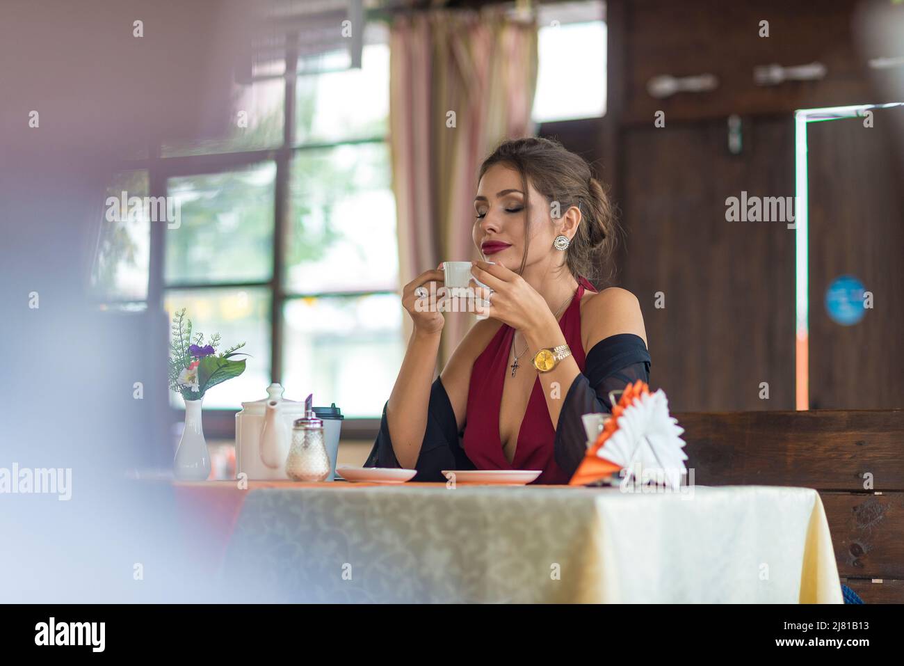 A stylish young woman drinks tea in a cafe - she sniffs a fragrant drink with pleasure. Stock Photo