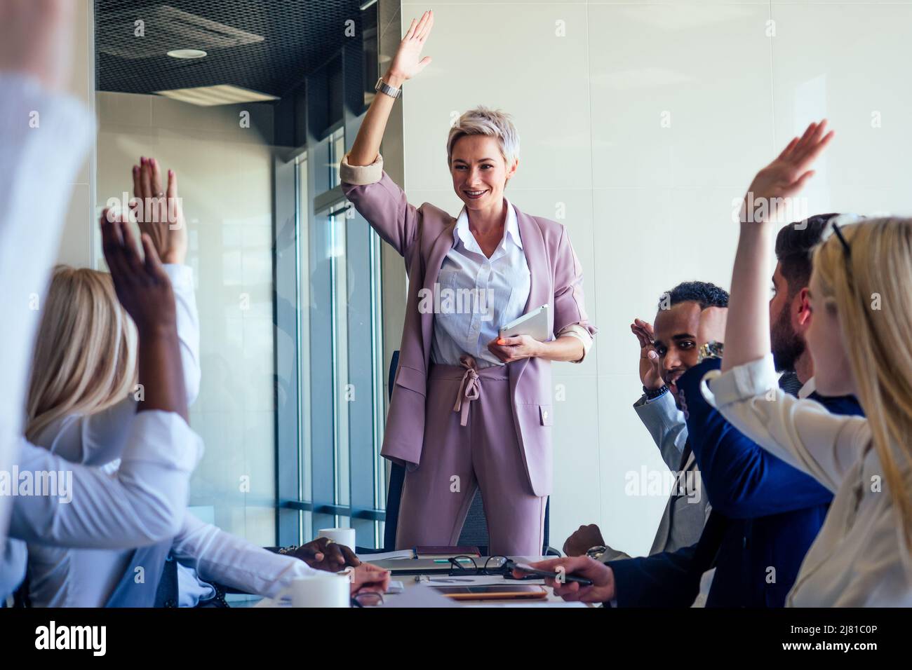 Business lady cheerful smile teacher or mentor coach speaking in front of group of colleagues raising hand up from different nationalities in modern Stock Photo