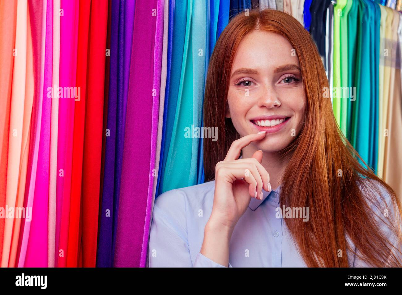 redhair ginger woman choosing color textile in tailor shop for new cloth sewing.she determines the colors that best suit an individual based capsule Stock Photo