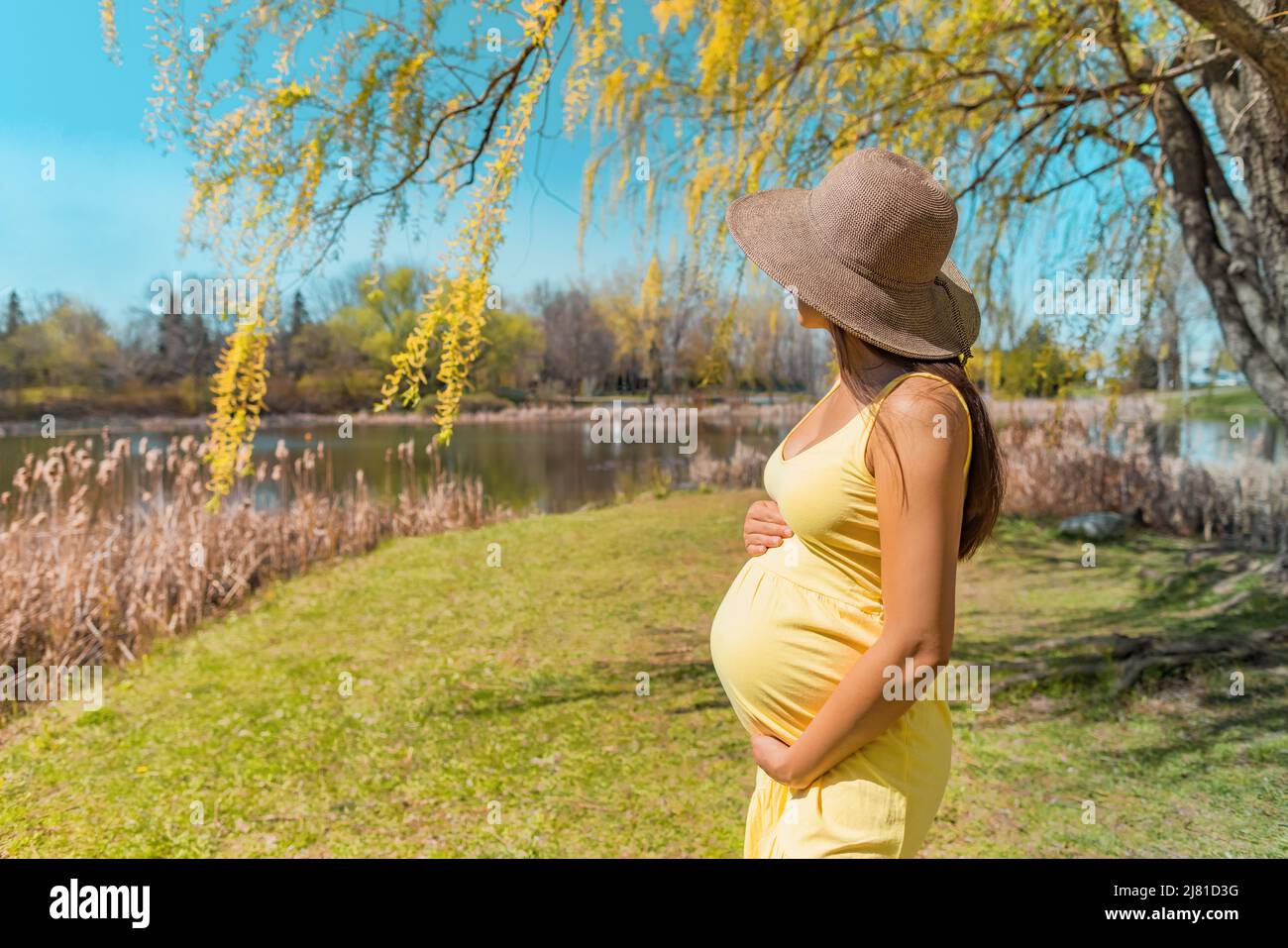 Pregnant woman walking in park wearing sun hat for skin solar protection against melasma skincare during summer. Pregnancy care Stock Photo