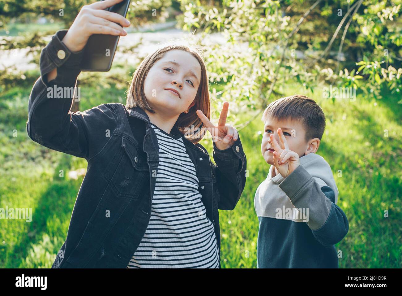 Preteen girl and schoolboy using camera of smartphone taking selfie at park at spring day. Stock Photo
