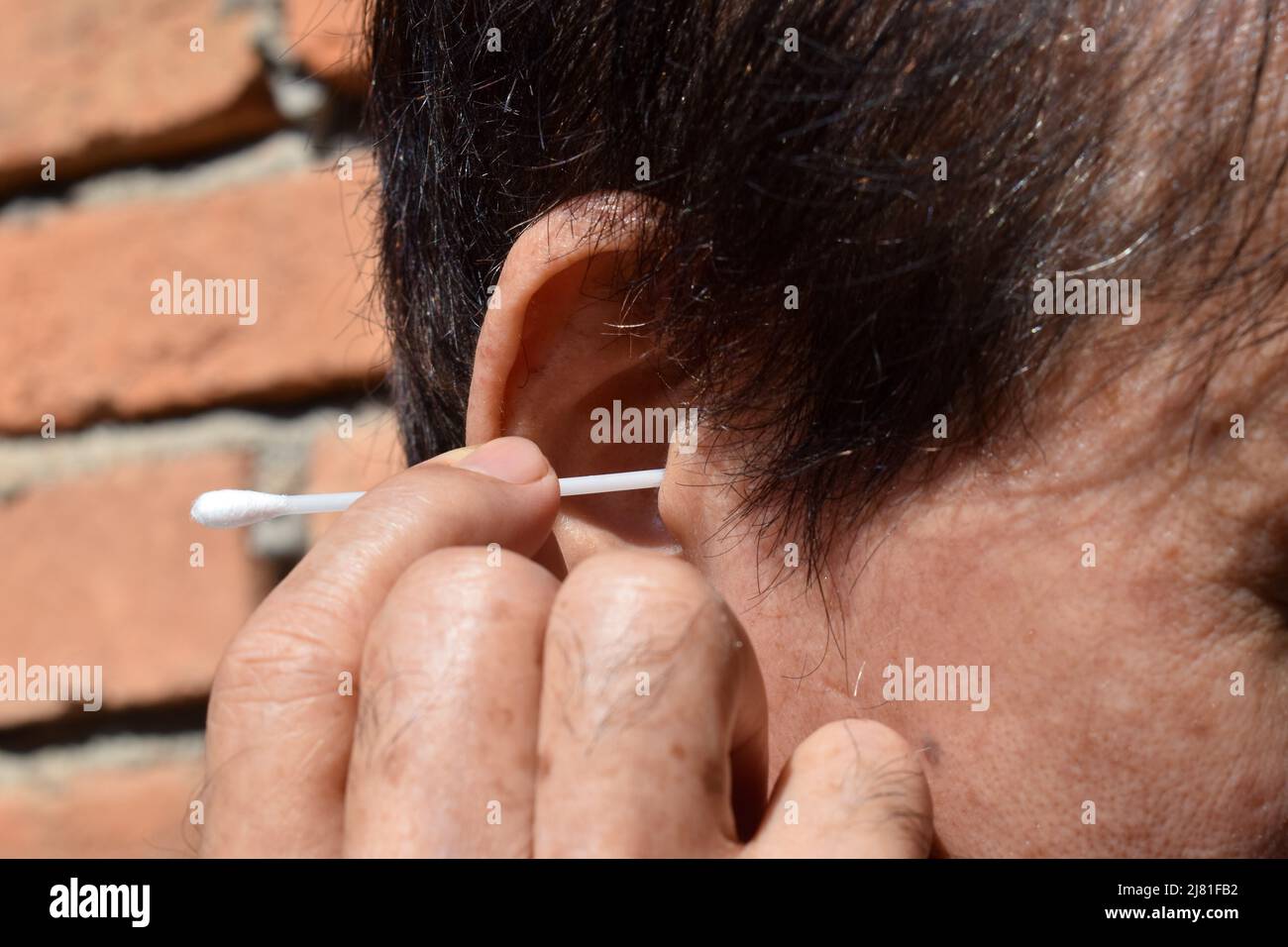 Asian old man cleaning his earwax with cotton earpick. Stock Photo