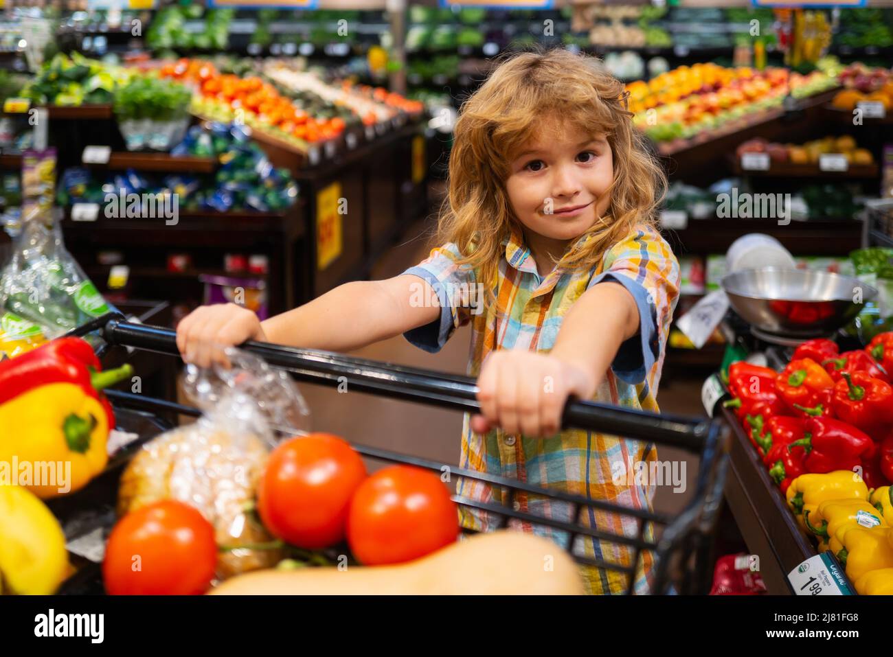 Child in supermarket buying fruit. Kid grocery shopping. Kid with cart choosing fresh vegetables in local store. Healthy kids food. Child in Stock Photo