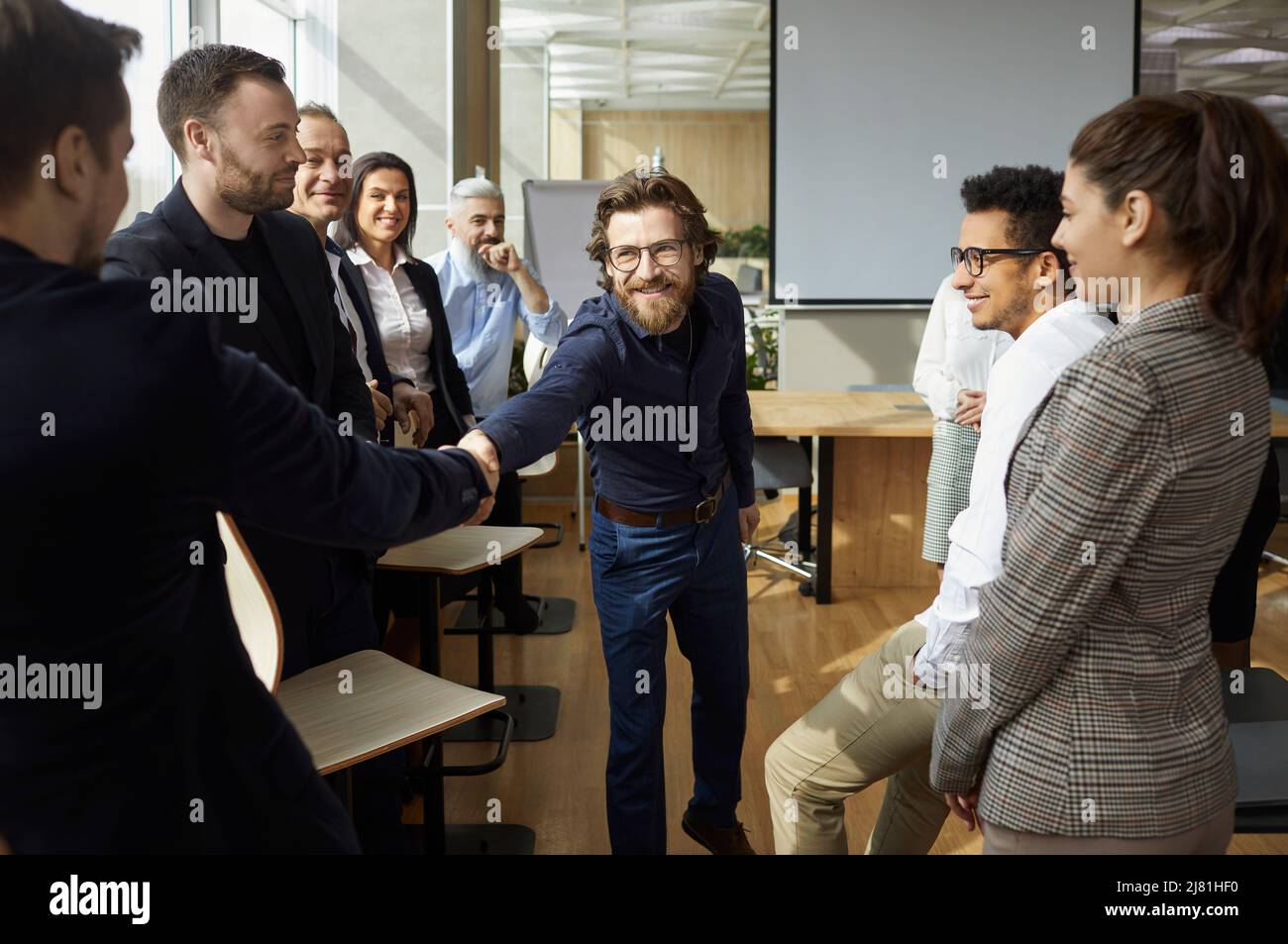 Friendly male colleagues shake hands during workplace meeting in modern coworking office. Stock Photo