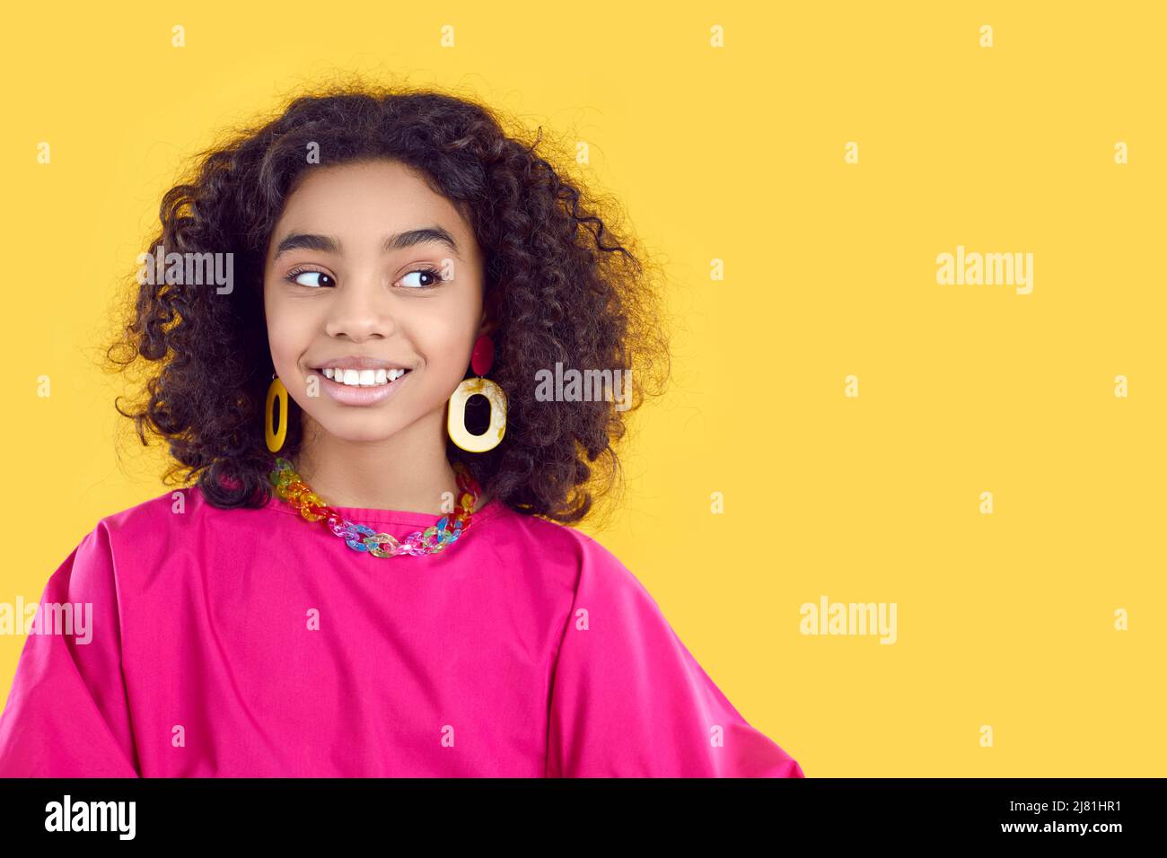 Beautiful African girl in trendy outfit looks at copy space on yellow background Stock Photo