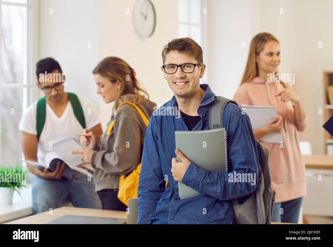 Smiling male student in classroom against background of classmates talking to each other. Stock Photo