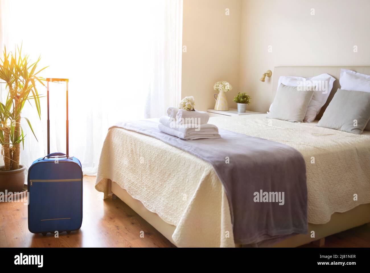 Very bright hotel room with clean white towels on the bed and suitcase