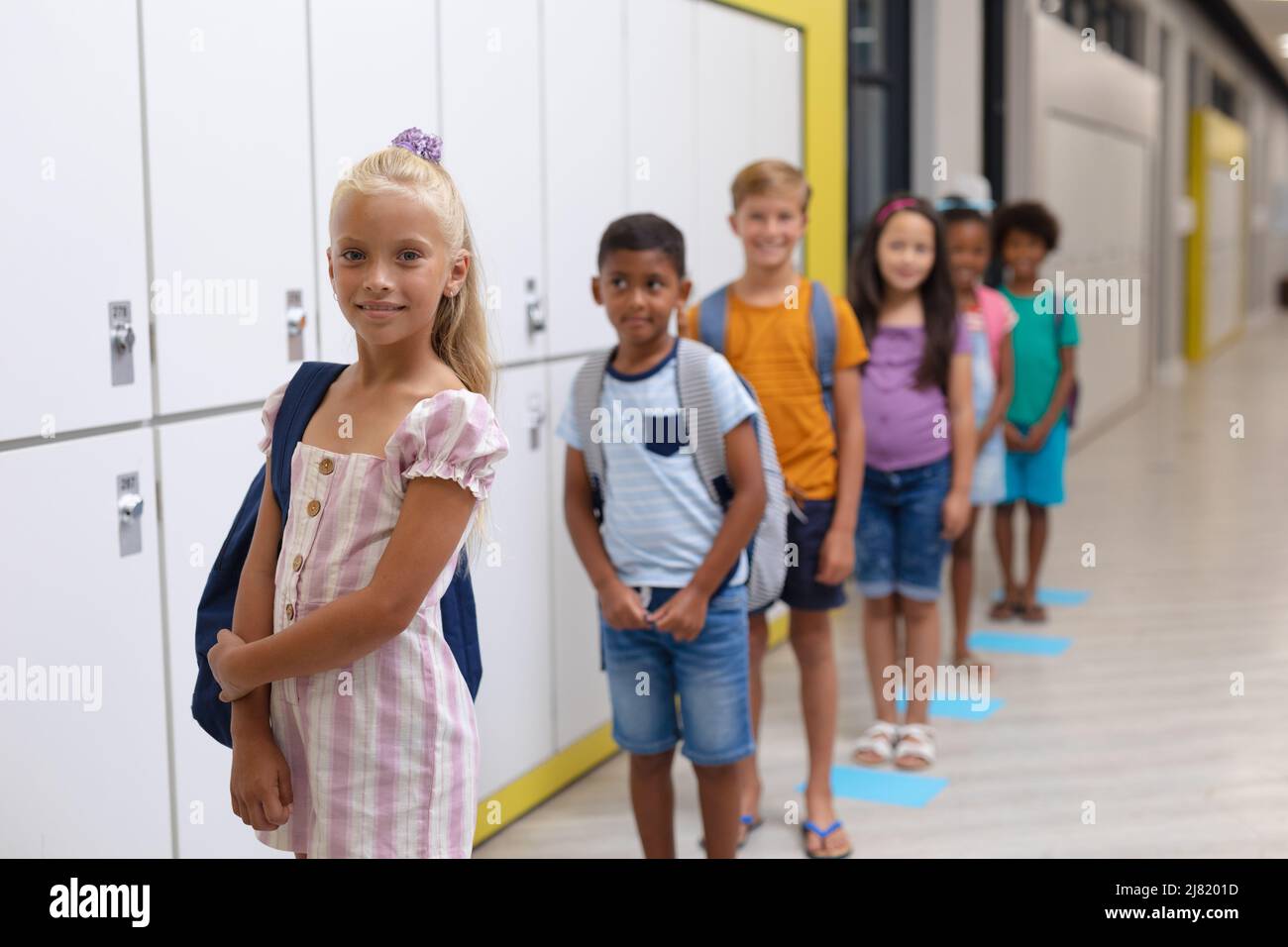 Portrait of caucasian elementary schoolgirl with multiracial classmates standing in row by lockers Stock Photo
