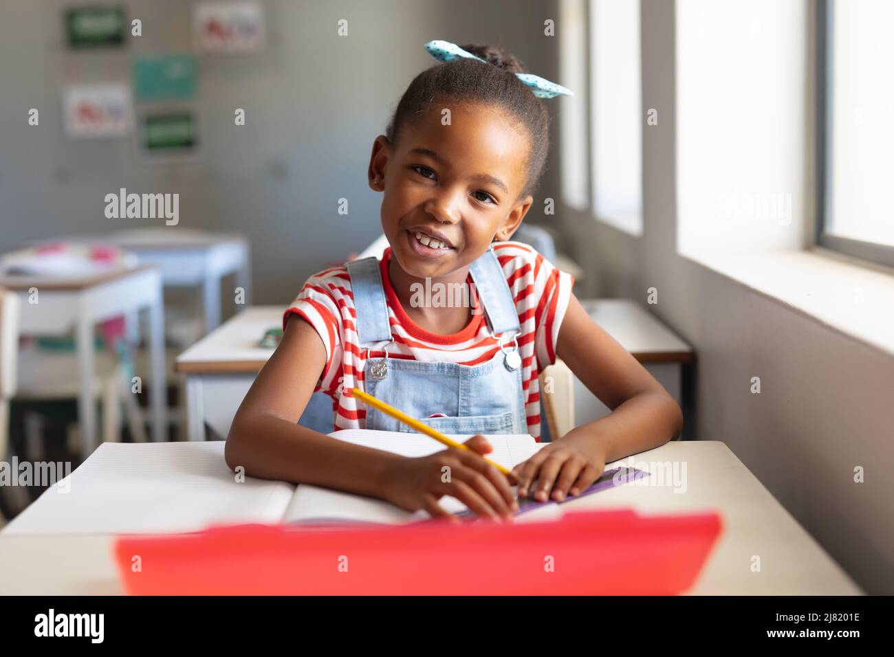 Portrait of smiling african american elementary schoolgirl with book ...