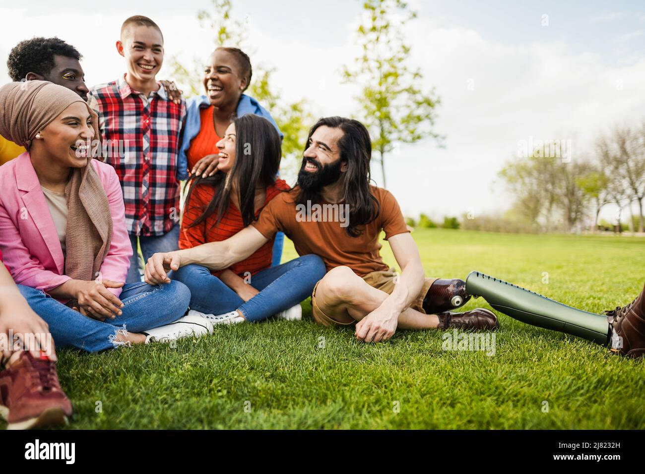 Multiethnic diverse people having fun outdoor sitting on grass at city park - Main focus on arabian girl face Stock Photo