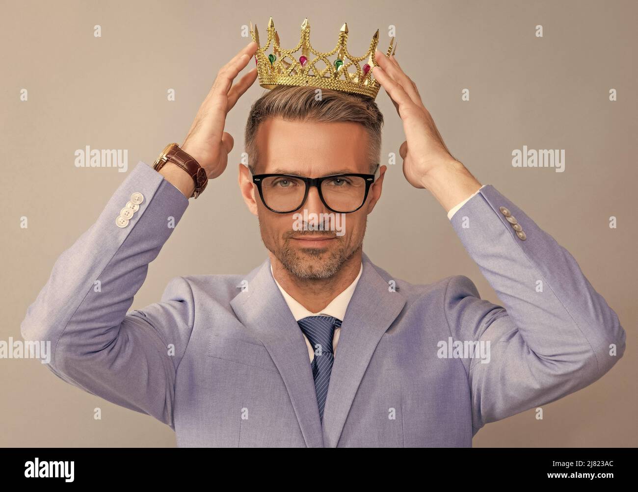 grizzled guy wearing king crown on grey background, success Stock Photo